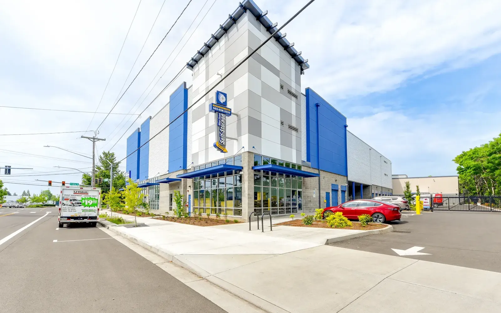 West Coast Self-Storage building in Clackamas, Oregon, with blue and gray facade panels, landscaped frontage, and street sidewalk.